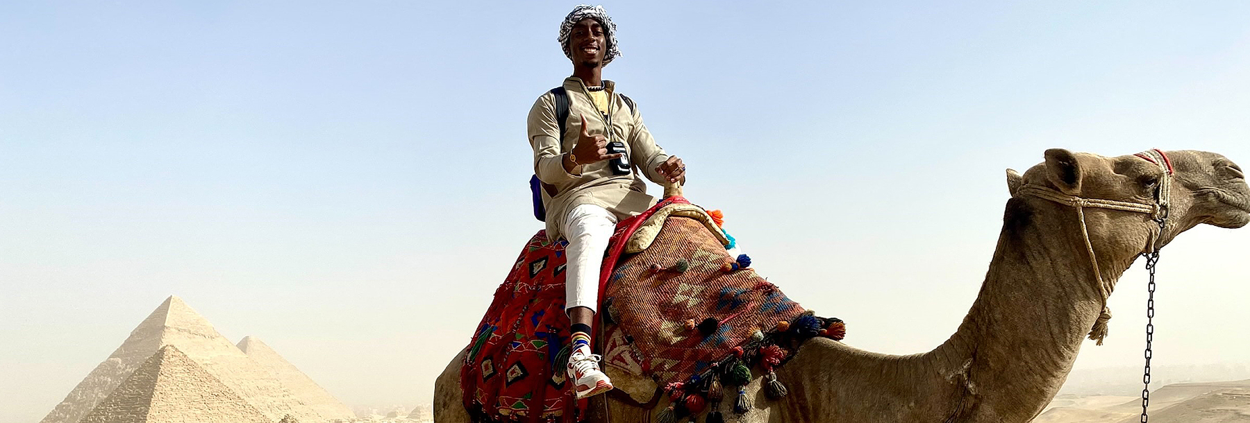 Section Image: Rasaan Hatcher riding a camel by the Pyramids 