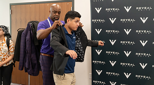 Section Image: Les Garrett addresses a group of students in the Neeley Banquet Room with a rack of suit coats in the back 