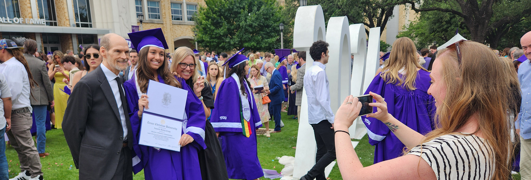 Section Image: Graduates take pictures in cap and gown with family outside of Schollmaier Arena 