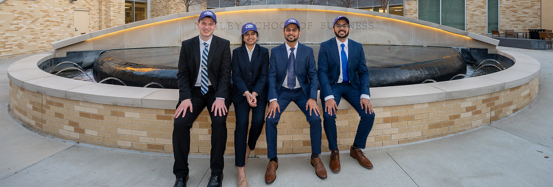 Section Image: University of Wisconsin team of Tobias Kern, Sajal Dixit, Saurabh Papppu and Juhi Goenka at the Neeley fountain wearing purple competition baseball hats 