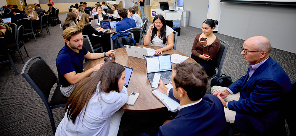 Students at round tables on laptops and phones