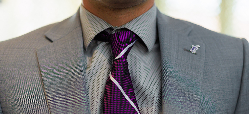 Section Image: Purple tie and horned frog lapel pin on a gray suit 