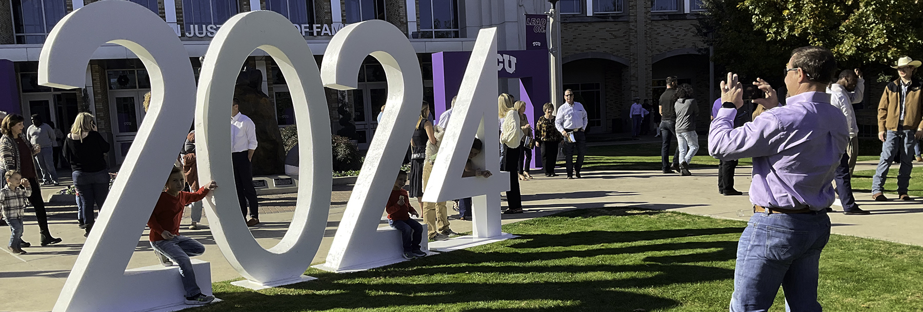 Section Image: Man taking picture of kids sitting on a huge 2024 in the lawn outside Schollmaier Arena 