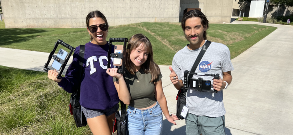 Three Mobile Journalism students pose with their phones in camera holders.