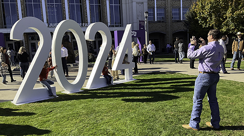 Man taking picture of kids sitting on a huge 2024 in the lawn outside Schollmaier Arena 