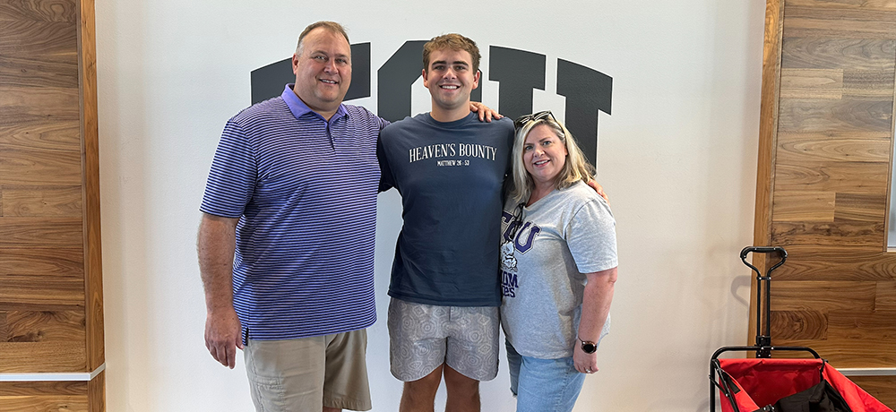 A son and his parents pose in front of TCU on the wall by Shaddock Auditorium