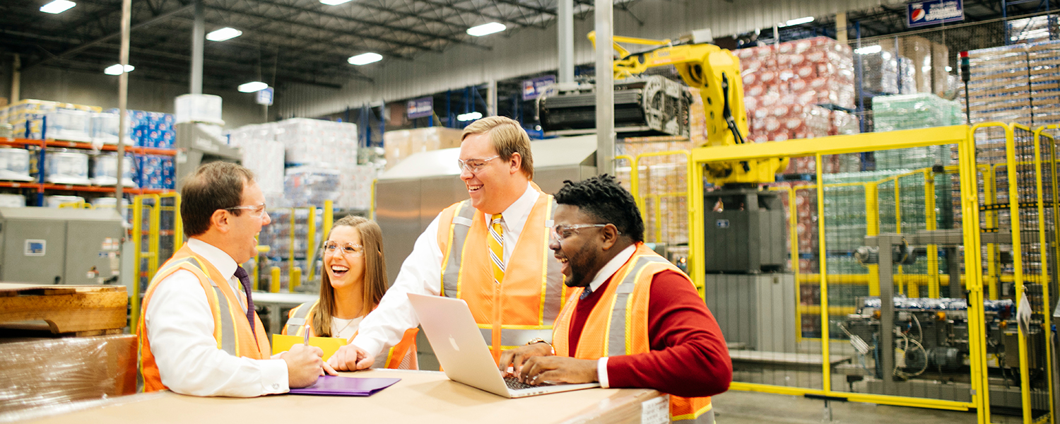 Four students inside a factory learning about supply chain operations