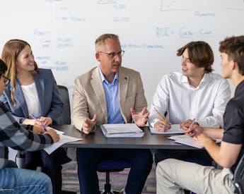 Faculty member leads a discussion with four students at a table