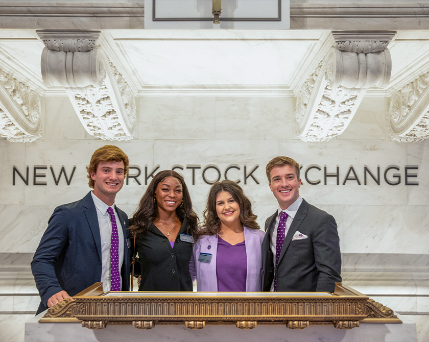 Four Neeley business students stand at the podium in the New York Stock Exchange