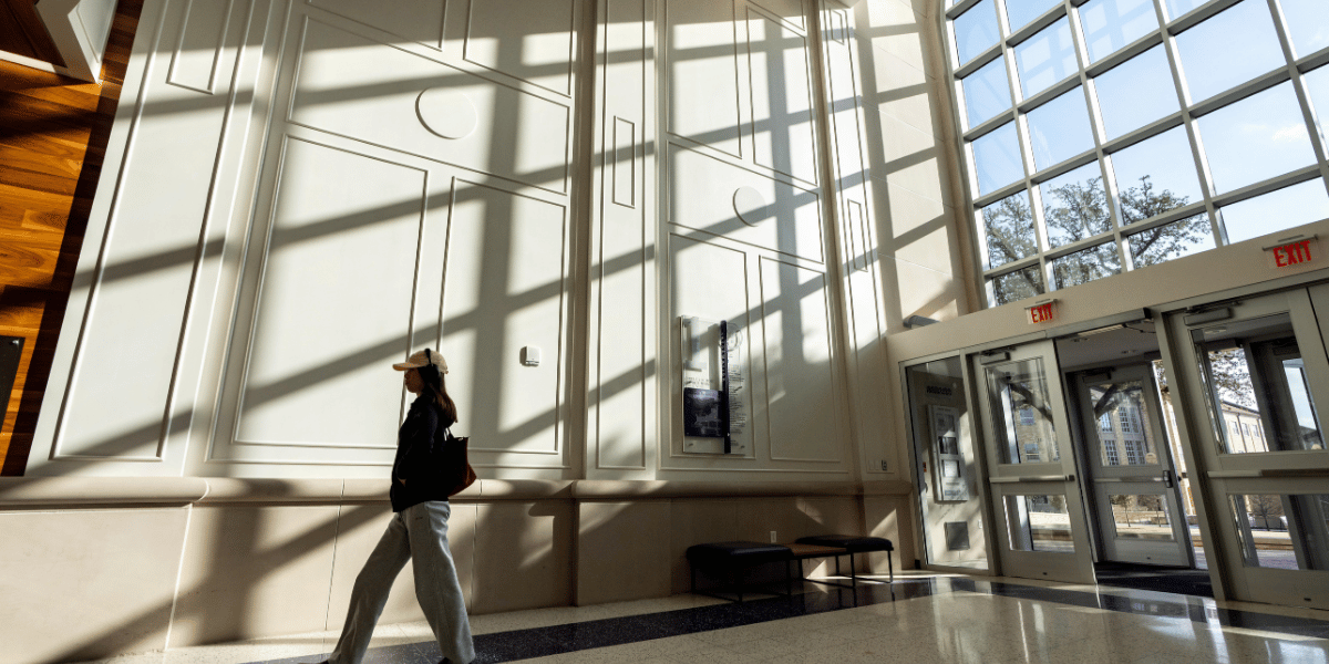 Student wearing a baseball cap and headphones is walking in Neeley entrance with shadows in the background.