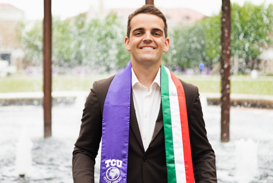 Undergraduate student wears graduation stole in front of Frog Fountain,
