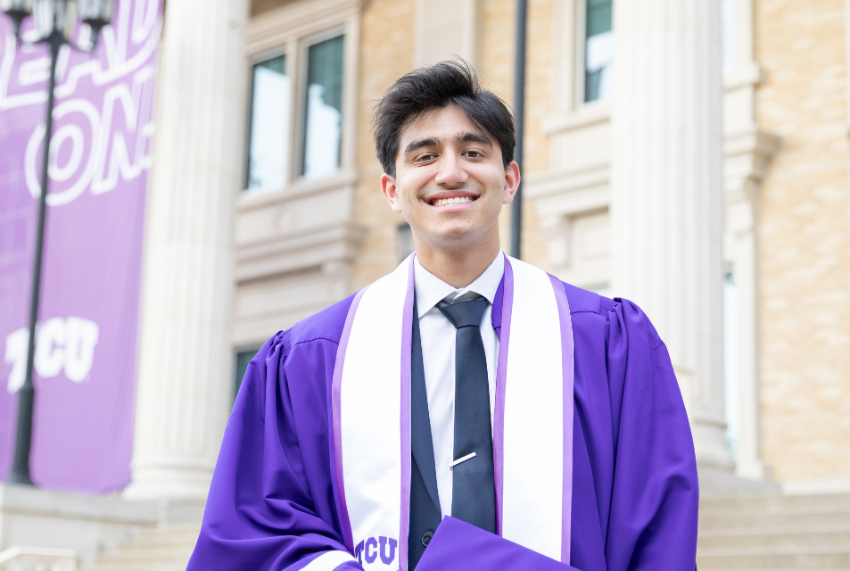 Student in graduation regalia in front of library.