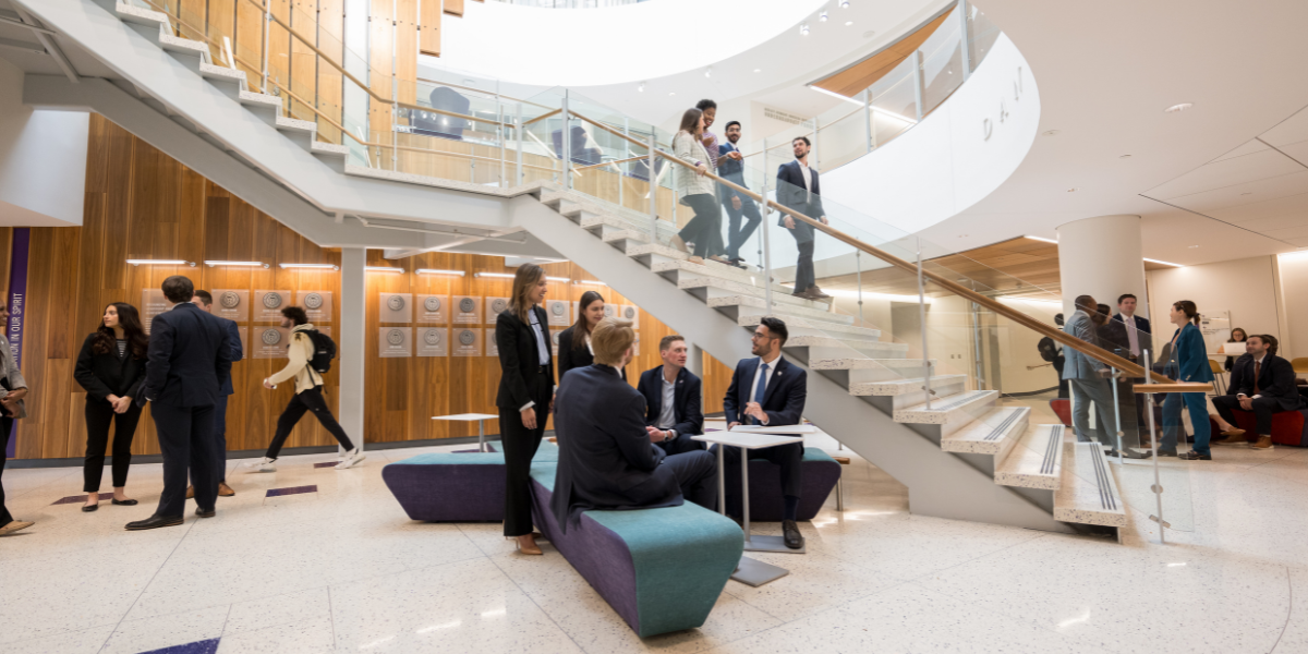 Clusters of students standing and walking at the base of the stairs in Dan Rogers Rotunda in the Neeley School of Business.